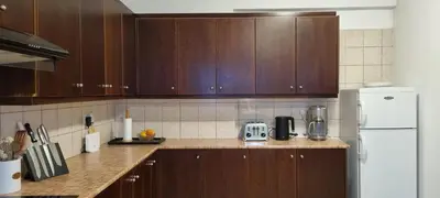 a kitchen with wooden cabinets and a white refrigerator at The Cozy Home Stay in Larnaca in Larnaka