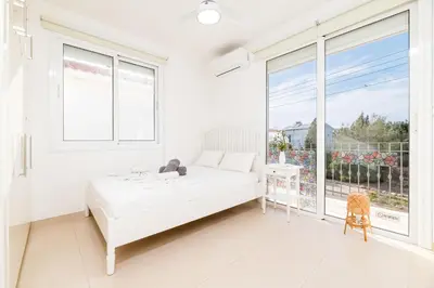 a white bedroom with a bed and a large window at Ayia Thekla Beach House in Ayia Napa