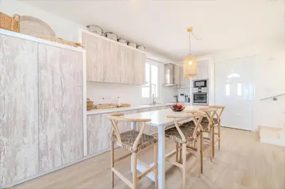 a white kitchen with a wooden table and chairs at Ayia Thekla Beach House in Ayia Napa