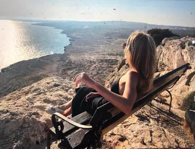 a woman sitting on a bench overlooking the ocean at Iliada Beach Hotel in Protaras
