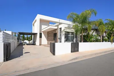 a white house with a fence and palm trees at Villa Evergreen - 3bed Bungalow large pool in Protaras