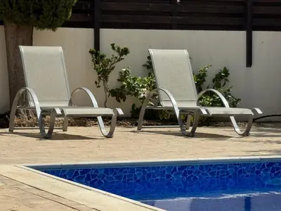 two white chairs sitting next to a swimming pool at Sunset Villa Agia Thekla in Ayia Napa
