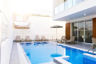 a swimming pool with chairs and umbrellas next to a building at Nissinest Luxury Villas in Ayia Napa
