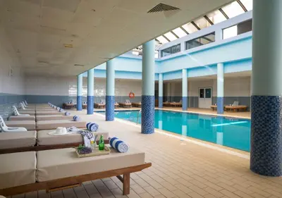 a pool with a row of beds in a large building at Constantinos the Great Beach Hotel in Protaras