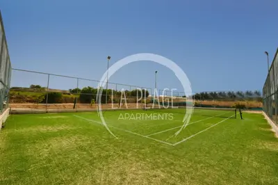 a tennis court with a net on a grass field at Cosy 2Br Family Apartment - Mythical Sands Resort in Paralimni