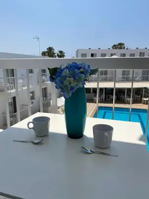 a vase with blue flowers sitting on a table with two cups at Mangoes & Cherries in Ayia Napa