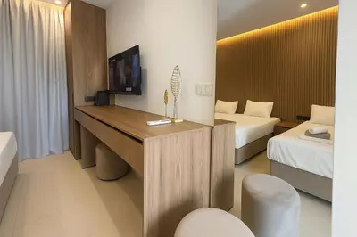 a hotel room with two beds and a desk with a television at NÓA Rooms - Adults Only in Ayia Napa