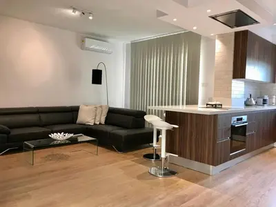 a living room with a black couch and a kitchen at Limassol Marina Seaview Suite in Limassol