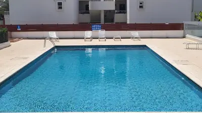 a swimming pool with chairs and a building at Hanapartment 3 bed Ayia NAPA in Ayia Napa