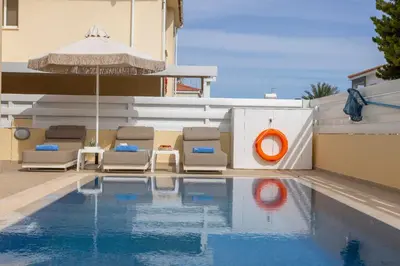 a pool with chairs and an umbrella next to a building at Villa Poseidon in Paralimni