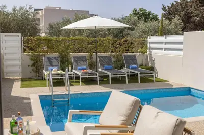 a pool with chairs and an umbrella next to a swimming pool at Milan's Mythical Villa in Paralimni
