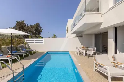 a swimming pool with chairs and an umbrella next to a building at Milan's Mythical Villa in Paralimni