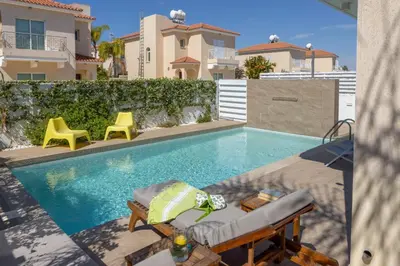 a swimming pool with two yellow chairs next to a house at Protaras El Sol Villa in Protaras