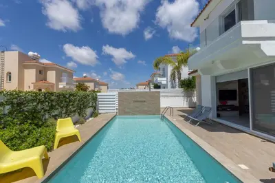 a swimming pool with two chairs and a house at Protaras El Sol Villa in Protaras