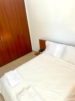 a bedroom with a bed with white sheets and a wooden cabinet at Seasons Retreat with pool and gym-2BR in Voroklini