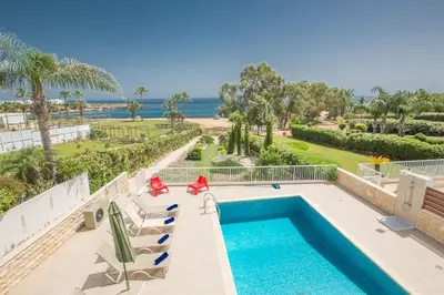 a pool with chairs and the ocean in the background at Protaras Mesogeios Villa Me16 Beachfront Villa in Protaras Center in Protaras