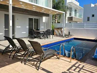 a patio with chairs and a table and a pool at Nissi beach villa Azure in Ayia Napa