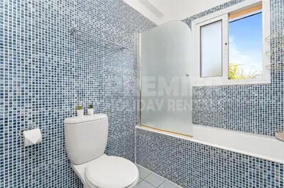 a blue tiled bathroom with a toilet and a window at Villa Coral in Paralimni