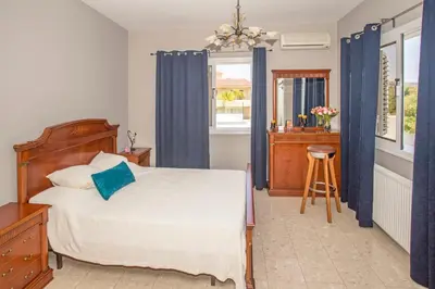 a bedroom with a bed with blue curtains and a stool at Nissi Maria Villa in Ayia Napa