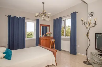 a bedroom with a bed with blue curtains and a tv at Nissi Maria Villa in Ayia Napa