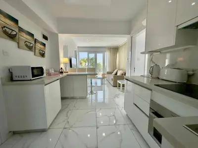 a kitchen with white cabinets and a living room at Lumière Retreat 2 in Larnaka