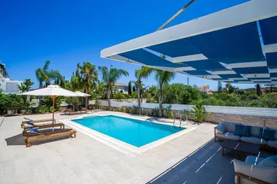 a swimming pool with a large blue umbrella and chairs at Pantio Living Villa in Ayia Napa