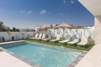 a swimming pool with chairs and umbrellas next to a fence at Orea Luxury Villas in Ayia Napa