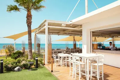 a patio with white tables and chairs and the ocean at Piere - Anne Beach Hotel in Ayia Napa