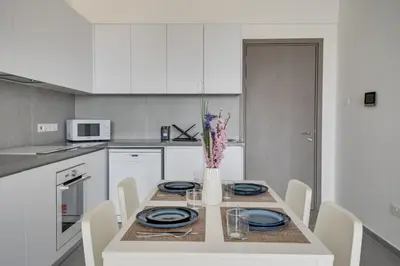 a white kitchen with a table with plates and a vase with flowers at Carisa Elysium Larnaca in Larnaka