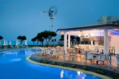 a restaurant with tables and chairs next to a swimming pool at Pernera Beach Hotel in Protaras