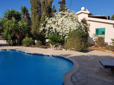 a swimming pool in front of a house with flowers at Konnos Villa in Protaras