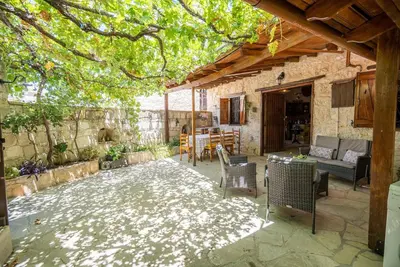 a patio with a table and chairs under a tree at Maison Des Vignes Lofou in Lofou