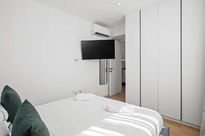 a white bedroom with a bed and a flat screen tv at Artemis 204 - Seaside Stories in Livadhia