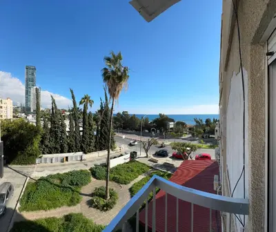 a balcony with a view of a street and a palm tree at Уютные Апартаменты с Балконом in Limassol