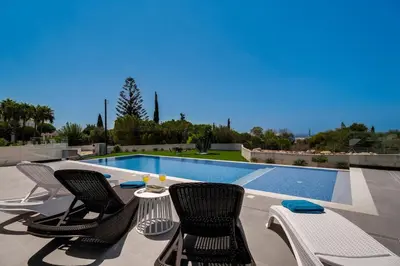 a pool with chairs and a table next to a swimming pool at Exclusive 7-Bdr Villa with Panoramic Views & Saltwater swimming pool! in Ayia Napa