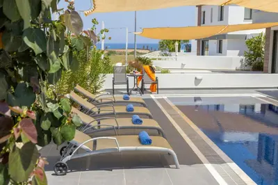 a row of chaise lounge chairs next to a swimming pool at Seaside Emerald in Paralimni