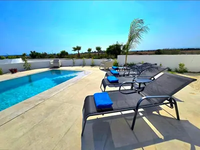 a row of lounge chairs next to a swimming pool at Larnaca Villa in Sophtadhes