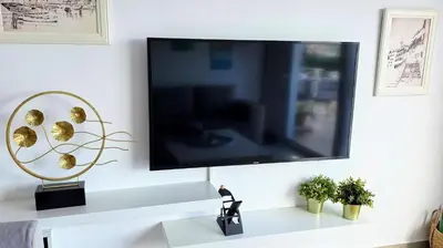 a flat screen tv hanging on a white wall at Amazing Sea View -3 Bed Ground Floor Garden Apartment in Kérynia