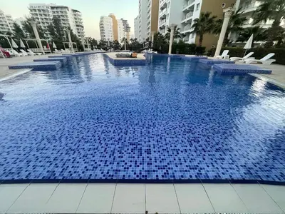 a large blue swimming pool with chairs and buildings at Family friendly modern flat in Caesar Resort &SPA, Long Beach İSKELE, KKTC in Iskele