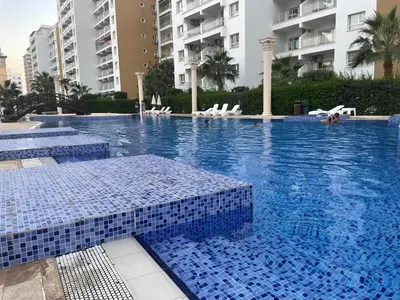 a swimming pool with blue tiles in a building at Family friendly modern flat in Caesar Resort &SPA, Long Beach İSKELE, KKTC in Iskele