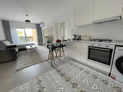a kitchen with white cabinets and a table with chairs at Family friendly modern flat in Caesar Resort &SPA, Long Beach İSKELE, KKTC in Iskele