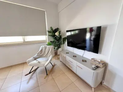 a white living room with a tv and a chair at Fresh & Cozy-close to the beach in Paralimni