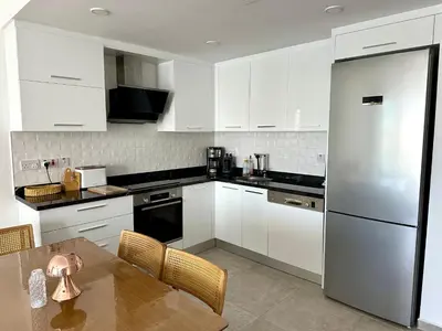 a kitchen with white cabinets and a table and a refrigerator at Bohemian penthouse in Girne Alsancak, close to Merit hotels in Kérynia