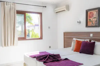 a bedroom with a bed with purple pillows and a window at Amethyst Napa Annex Apartments in Ayia Napa