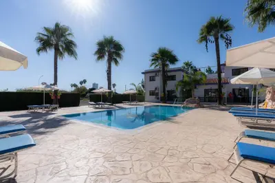 a swimming pool with chairs and palm trees at Amethyst Napa Annex Apartments in Ayia Napa