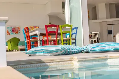 a swimming pool with colorful chairs and a table at Protaras Seafront Villa AleMar in Protaras