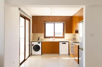 a kitchen with wooden cabinets and a washer and dryer at Spacious & Bright Apartment with Balcony in Larnaka