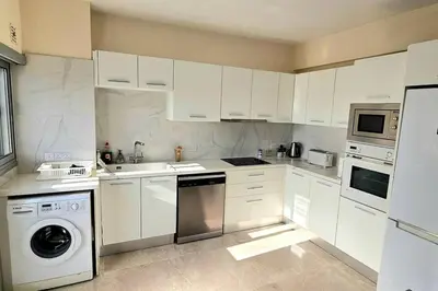 a kitchen with white cabinets and a washer and dryer at Dasoudi Pecora Beach Apartment in Limassol