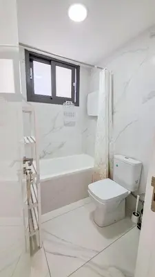 a white bathroom with a toilet and a bath tub at Pool Citylux Apartment in Larnaka