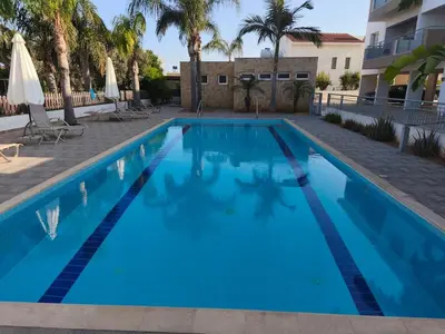 a large blue swimming pool with palm trees and a building at Harmonia Home in Paralimni